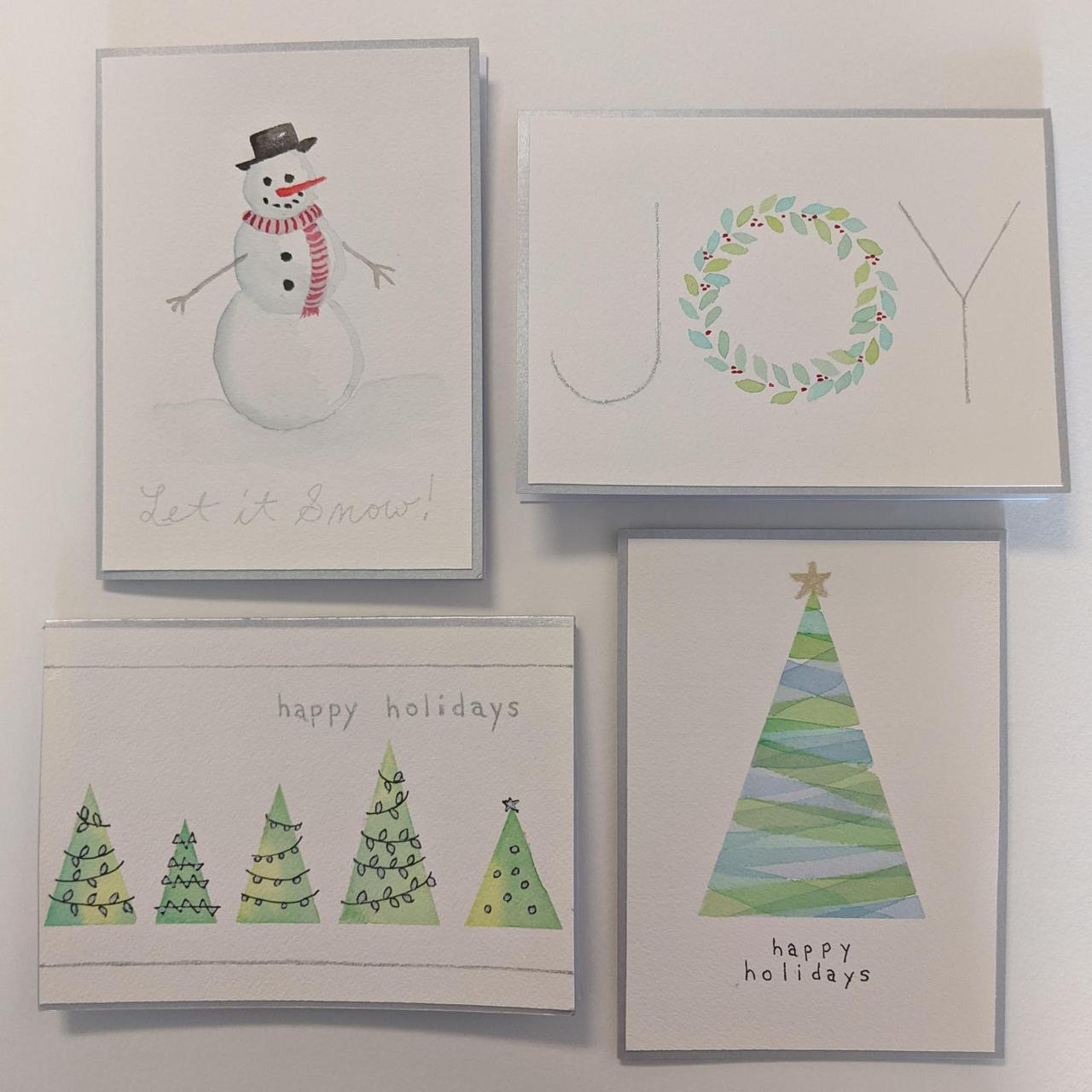all four holiday cards in a grid, going counter clockwise from the upper left, the cards picture a snowman, the word "JOY", a single christmas tree, and a row of christmas trees.