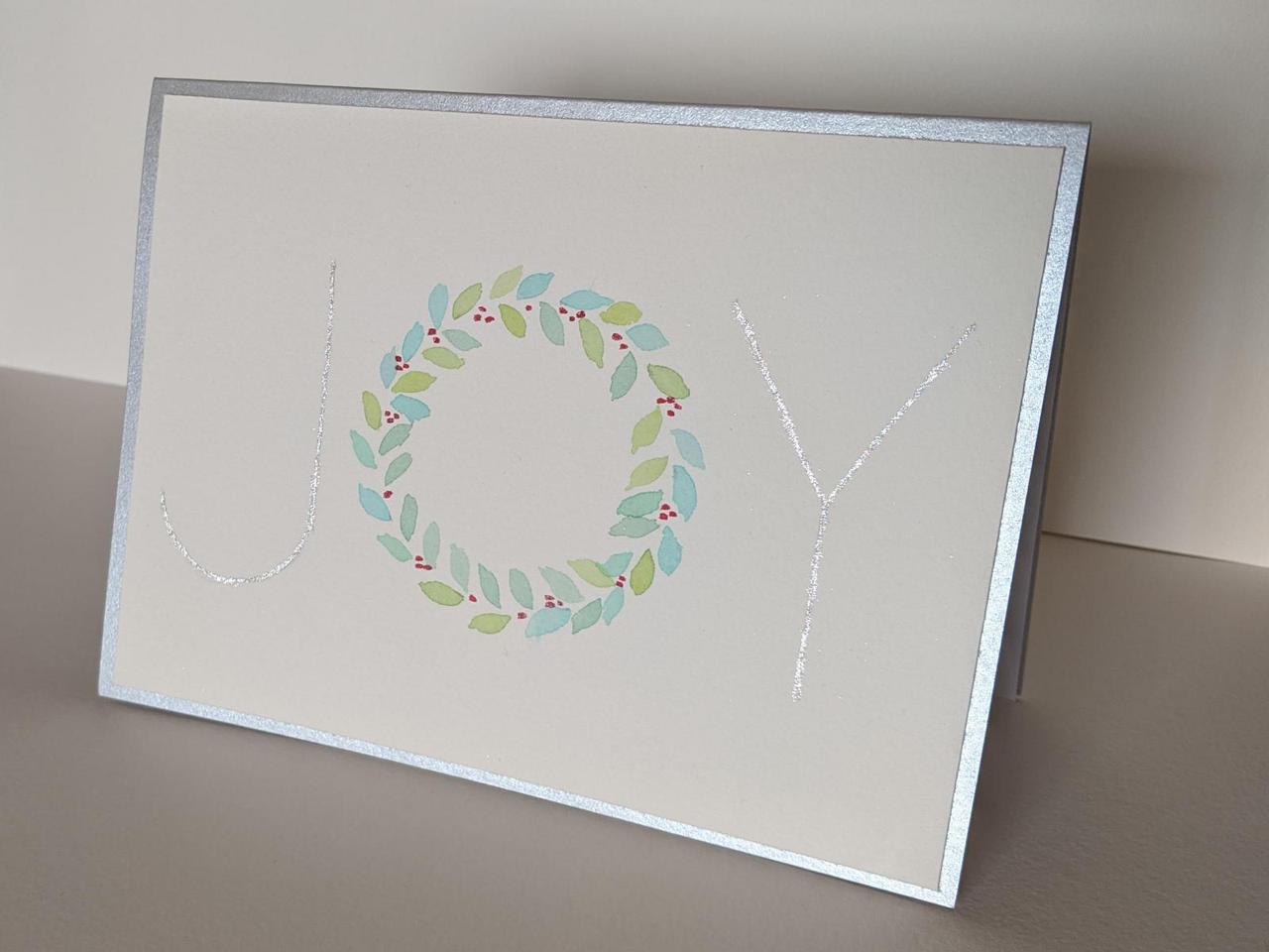 holiday card that has the word JOY on the front, with the letter "O" replaced with a wreath.