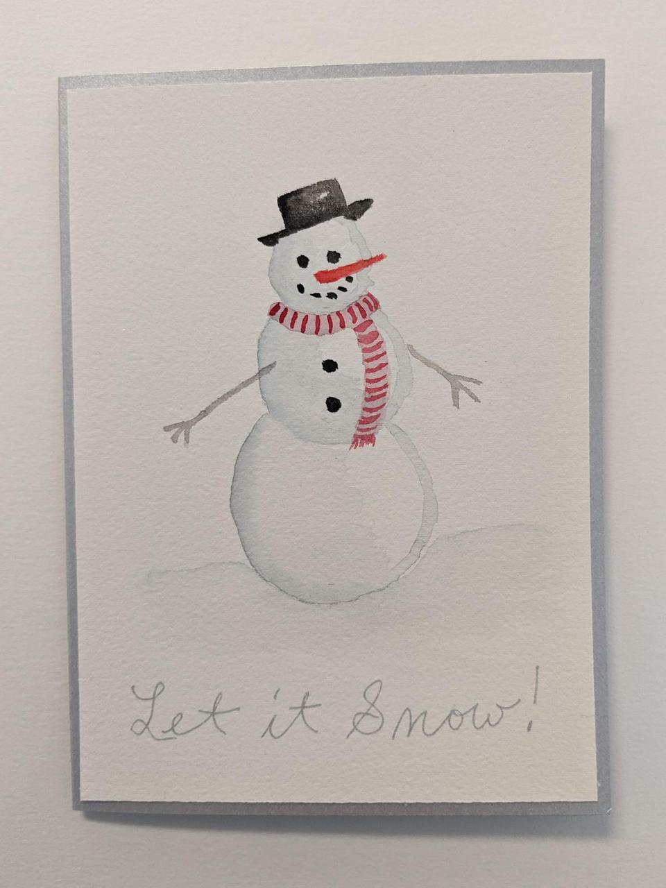 holiday card with a painting of a snowman on the front, with a carrot nose and coal eyes and mouth. It says "Let it Snow" across the bottom.