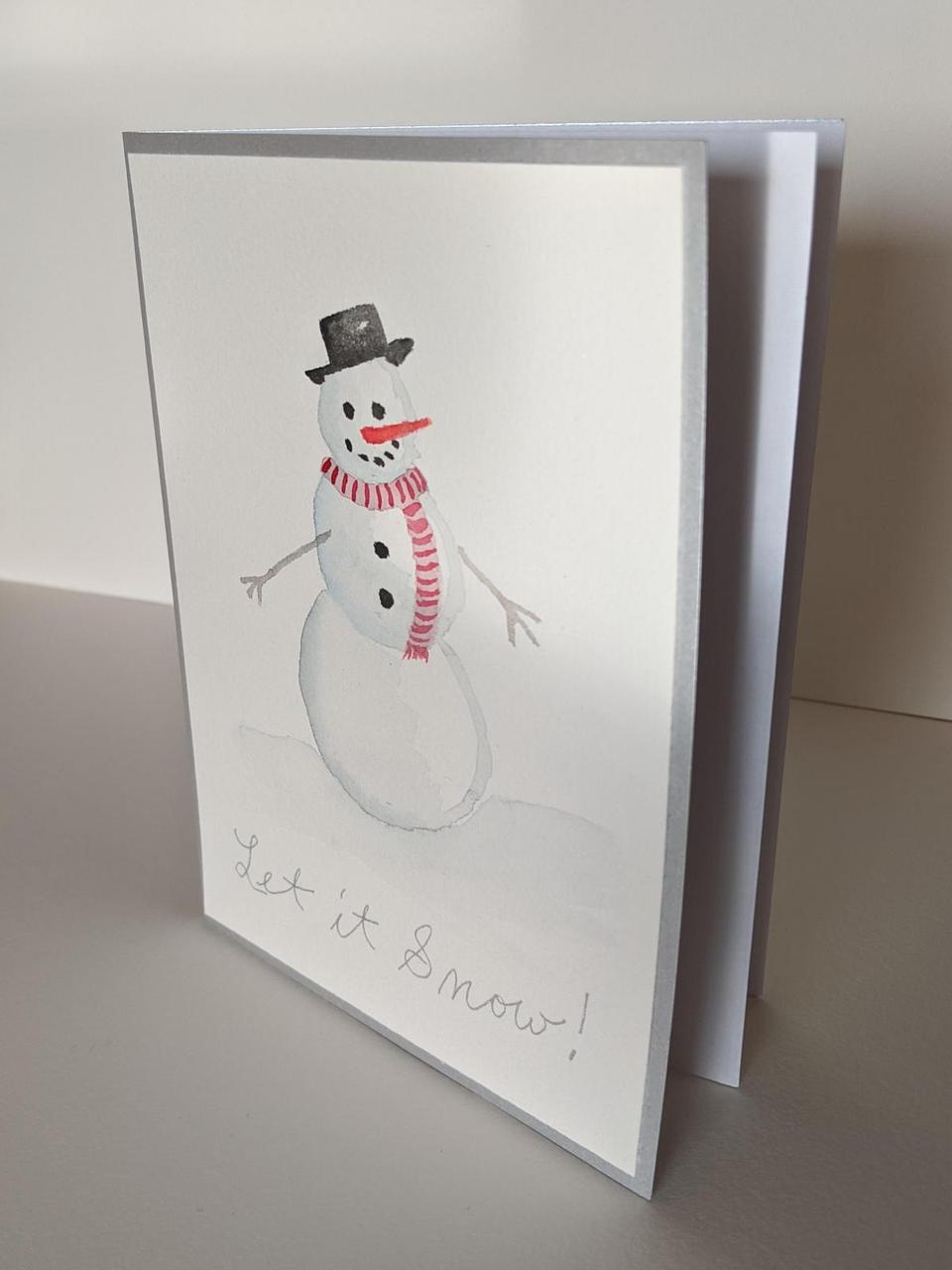 holiday card with a painting of a snowman on the front, with a carrot nose and coal eyes and mouth. It says "Let it Snow" across the bottom.