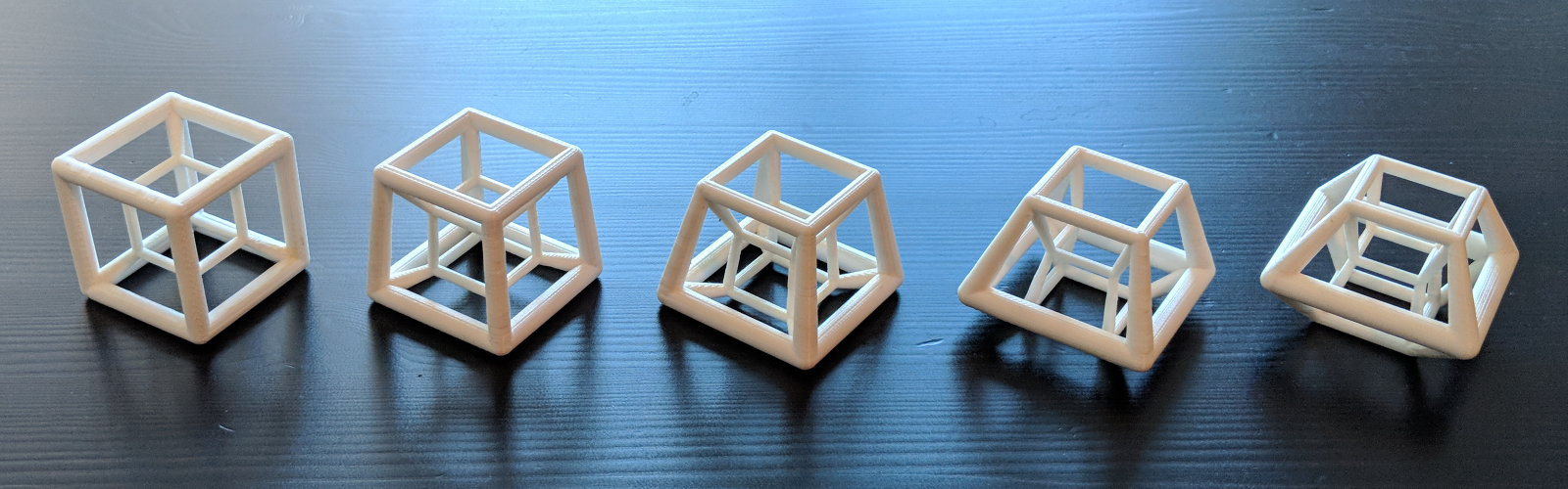 series of five printed hypercubes in a row, sitting on a wooden table.