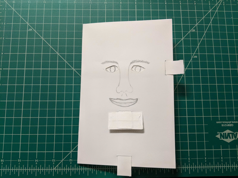 Animation showing a few states of the paper human face, drawn with pencil. It is looking straight ahead, to the right, and to the left. When looking to the left it has a sad mouth orientation.