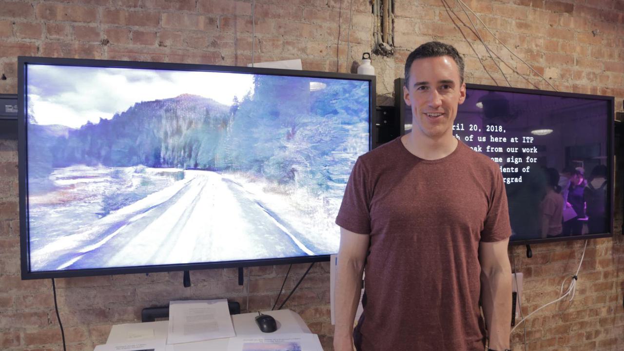 Me standing in front of a computer monitor displaying an animation moving down a highway with a river to the left and trees to the right and clouds in the background.