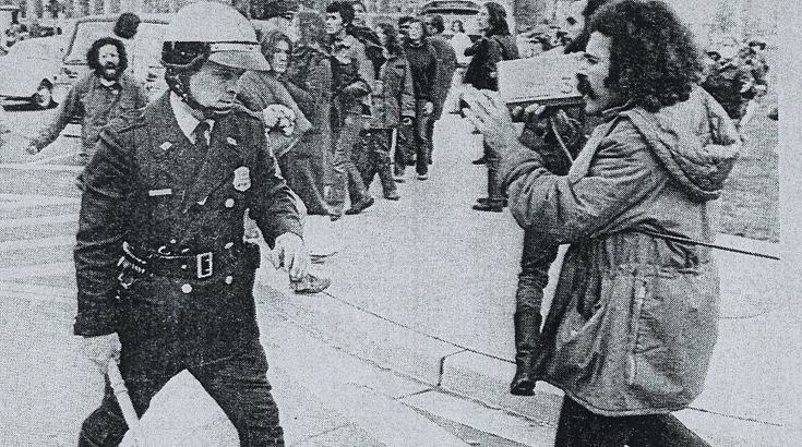 man with video camera about to be hit by police officer