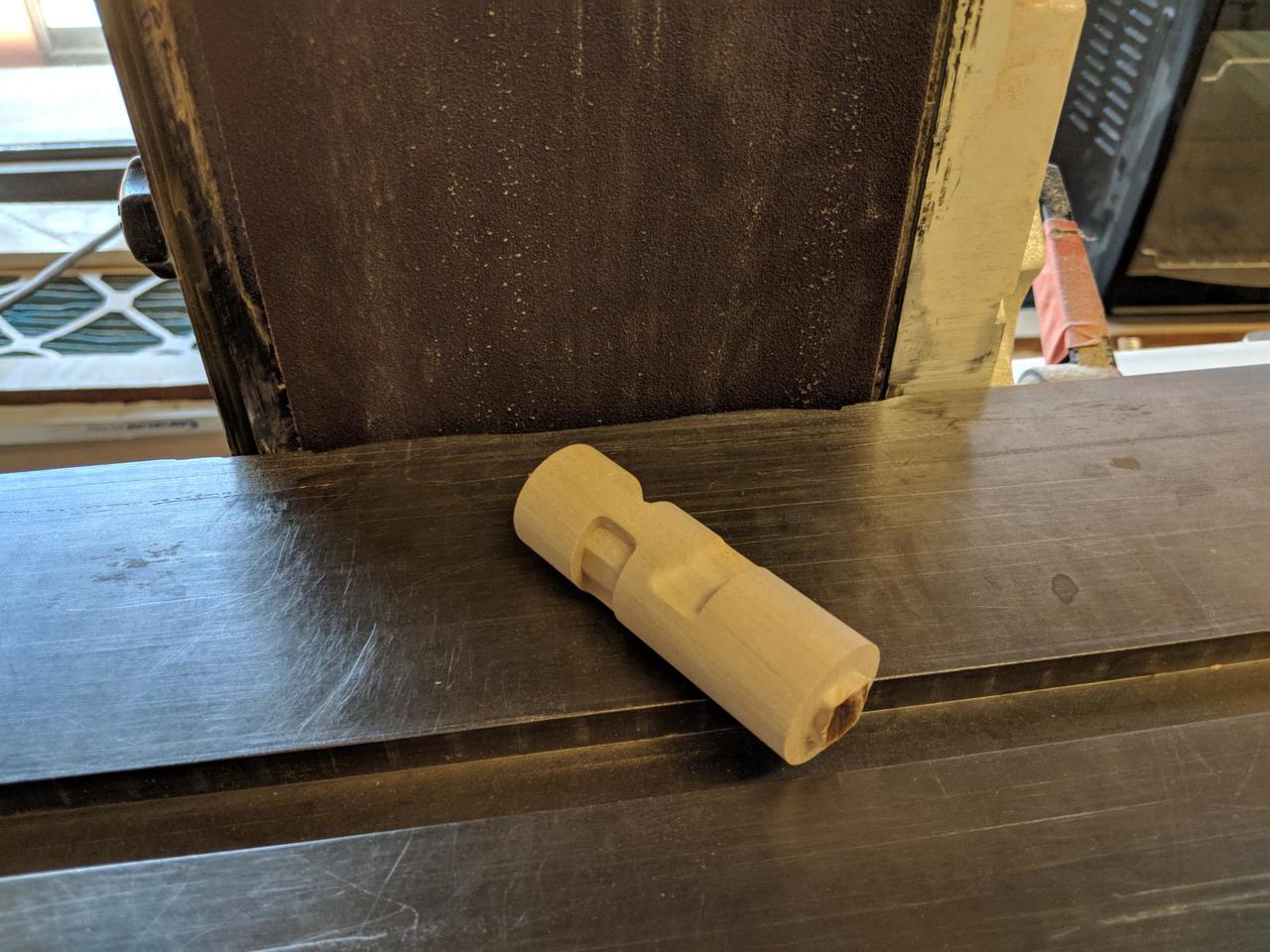 cylinder piece of wood sitting on metal bed with belt sander right behind it.