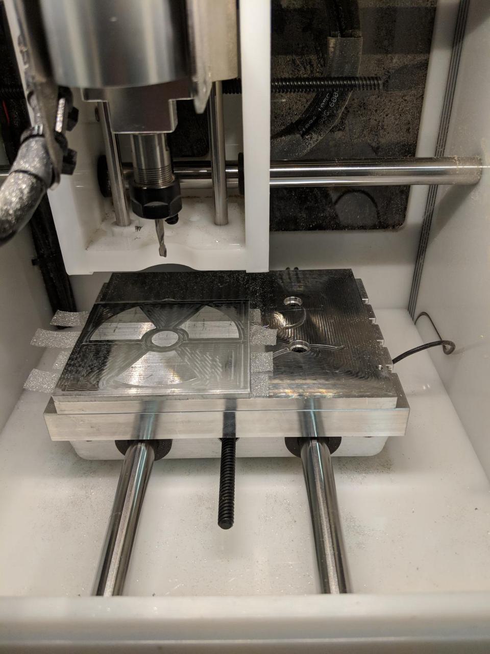 aluminum square in othermill container with drill bit hovering above it.