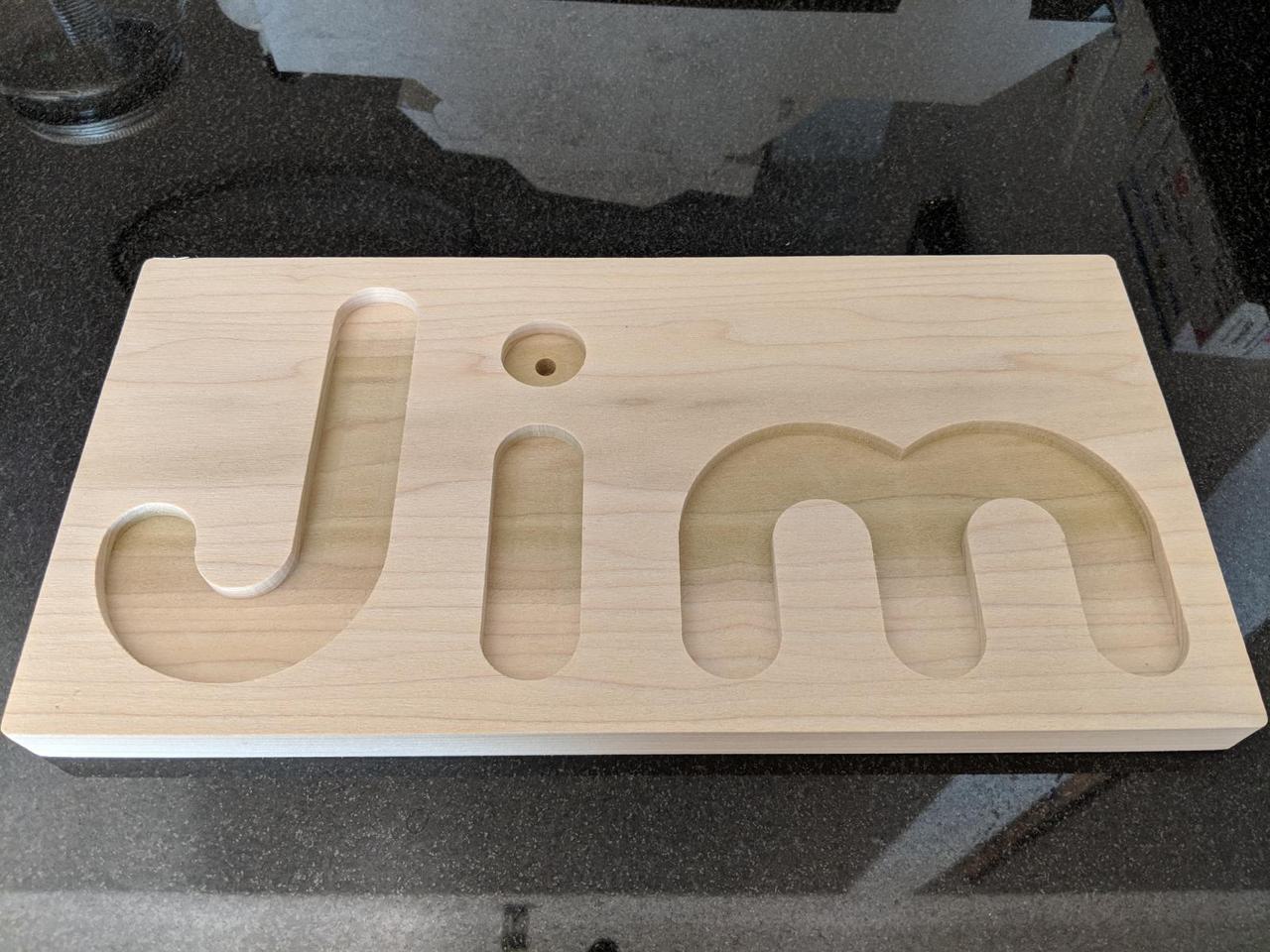 rectangular piece of wood with the letters J I M carved into it.