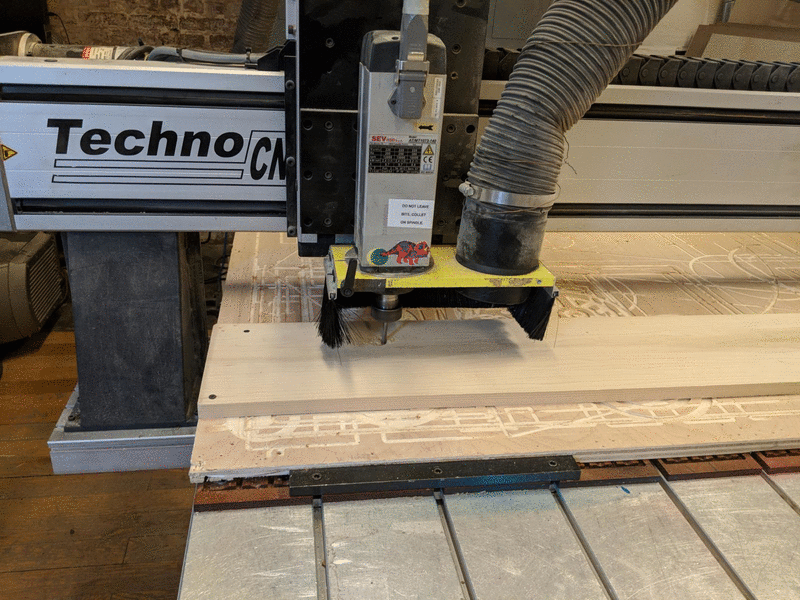 CNC using a drill-like device to carefully carve into a piece of wood that has been screwed down into a larger piece of wood.