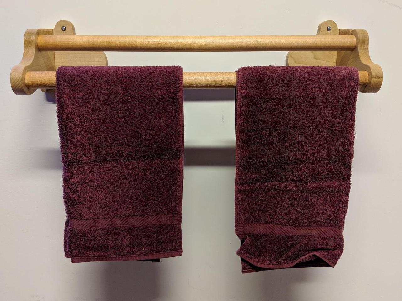 wooden towel rack mounted on the wall with two hand towels hanging on it.