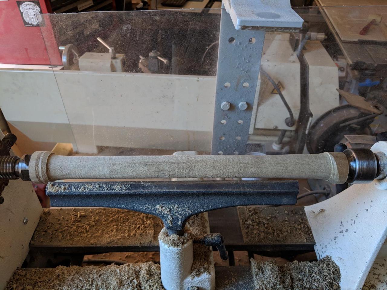 wooden cylinder mounted in wood lathe, with straight carved surface.