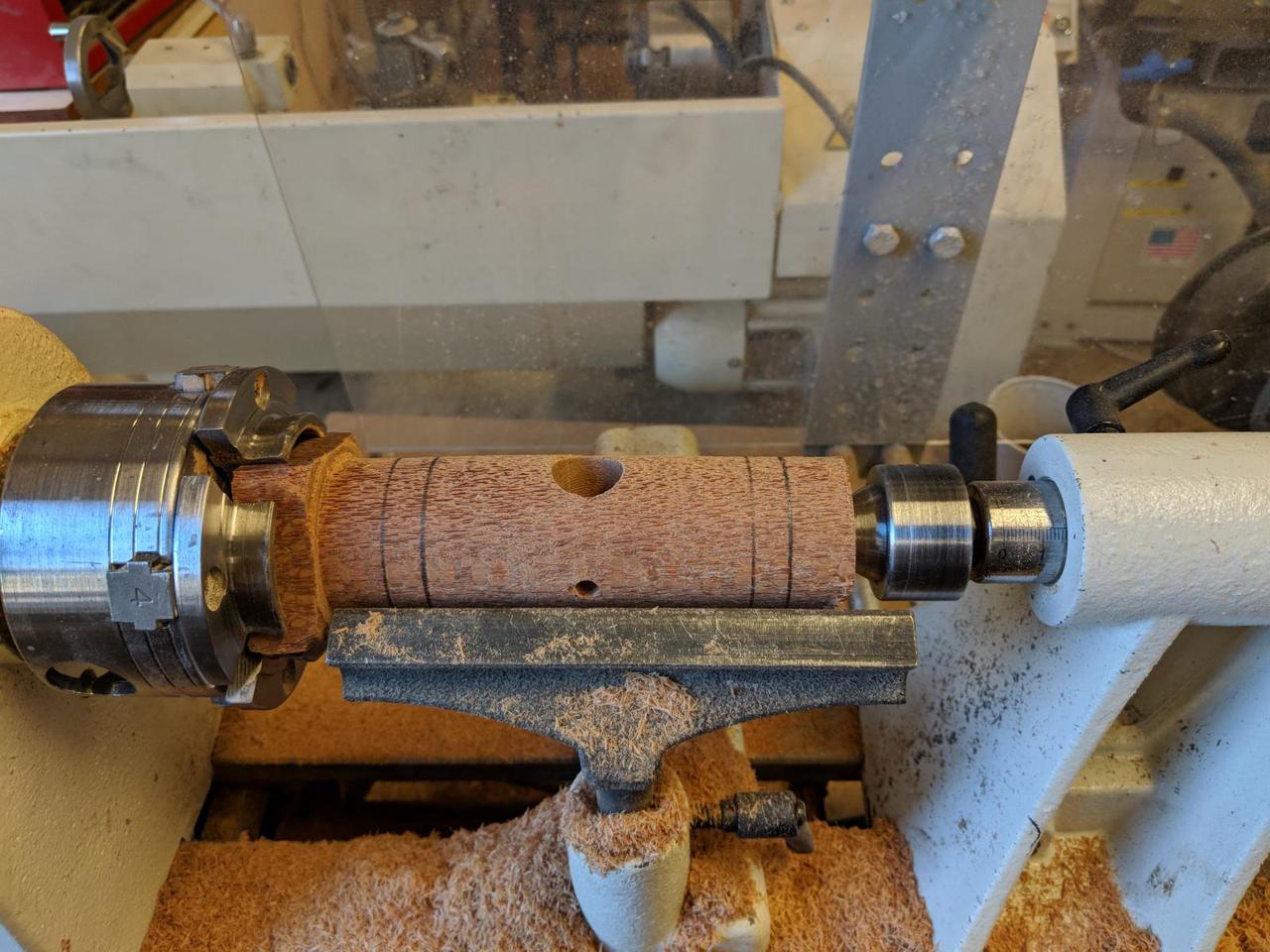 lacewood cylinder mounted on wood lathe with pencil marks drawn around circumference in four places.