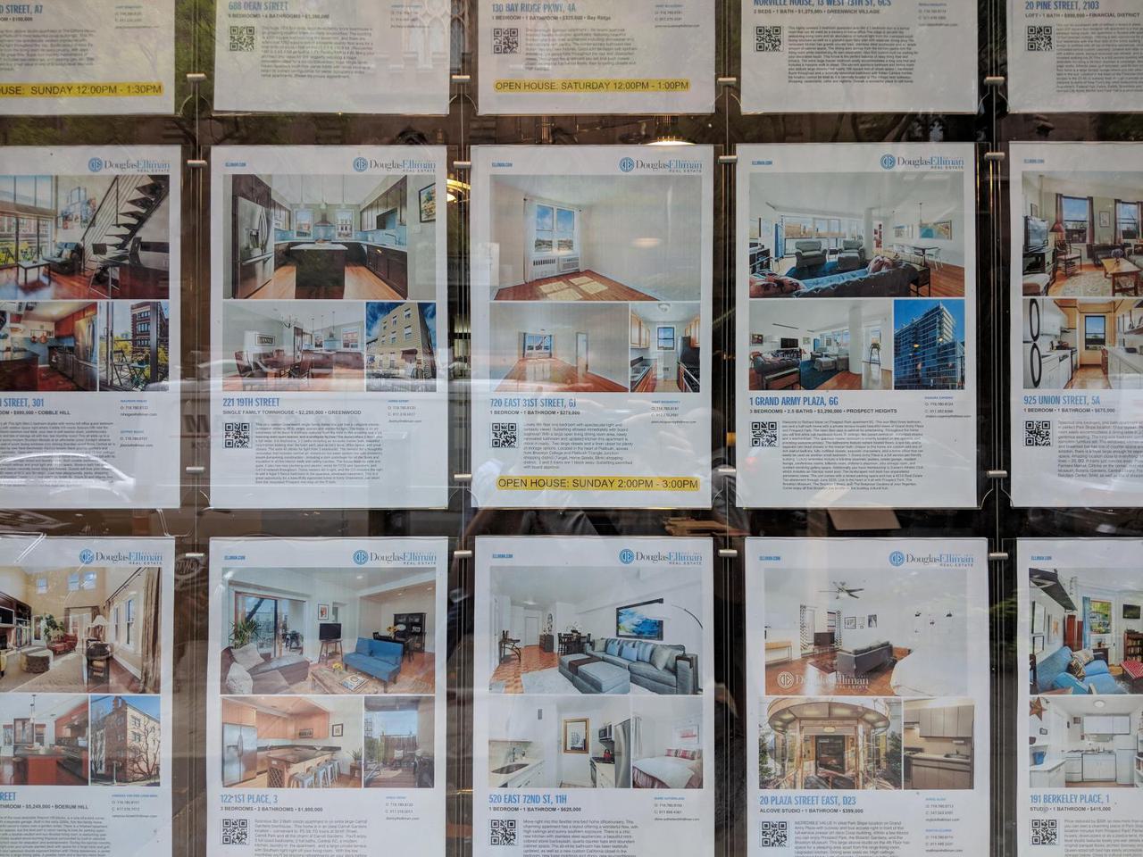 fifteen apartment posters in real estate office window, each displaying a photo of the apartment with the price and relevant apartment information.