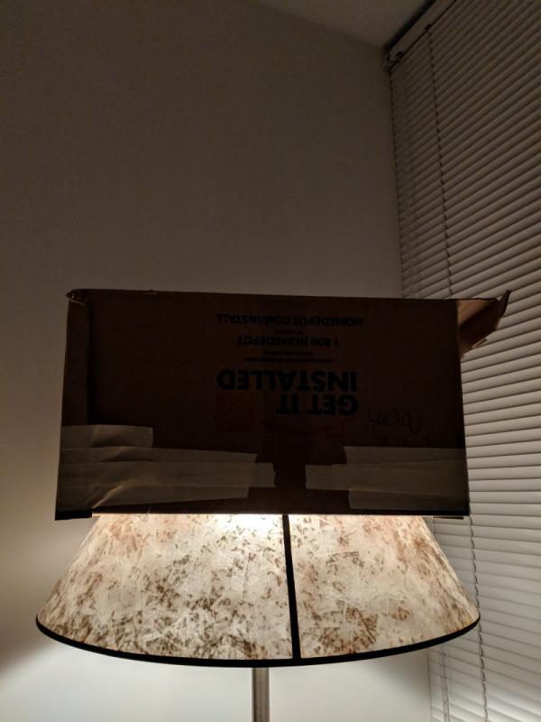 Standing lamp with cardboard cover on top, blocking light from hitting the wall and venetian blinds