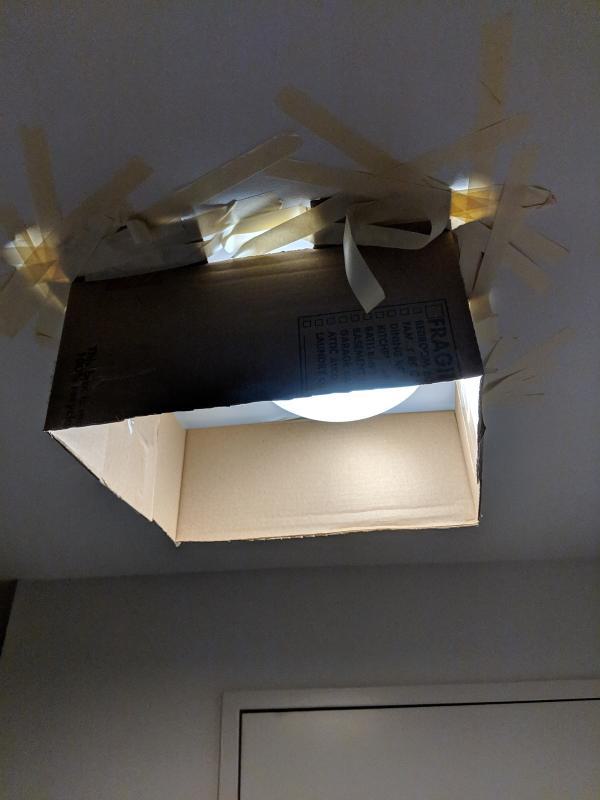 Ceiling light with cardboard hanging from edges, blocking light from hitting the ceiling and door