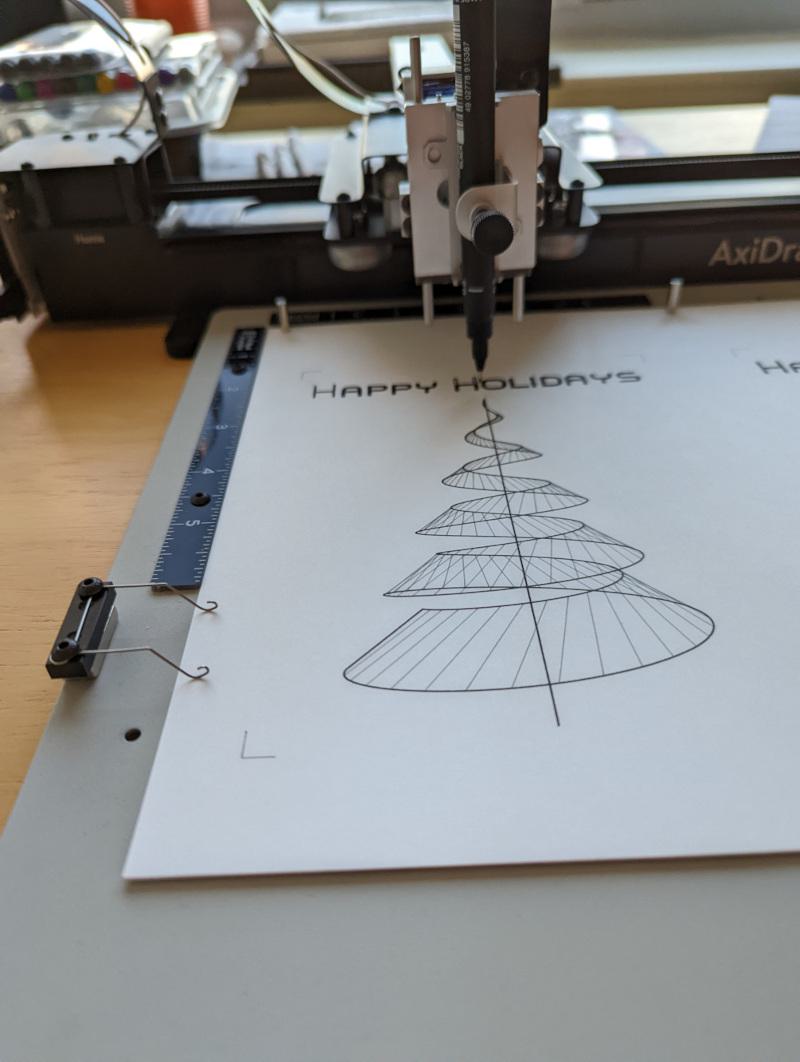 axidraw pen plotter drawing a wire frame christmas tree and the words "happy holidays" across the top