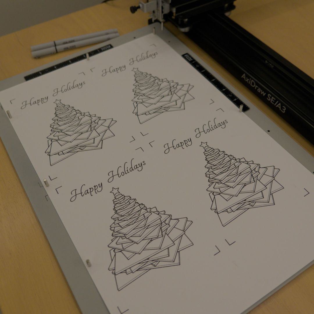 axidraw pen plotter drawing four christmas tree cards and with the words "happy holidays" or "merry christmas" across the top of each