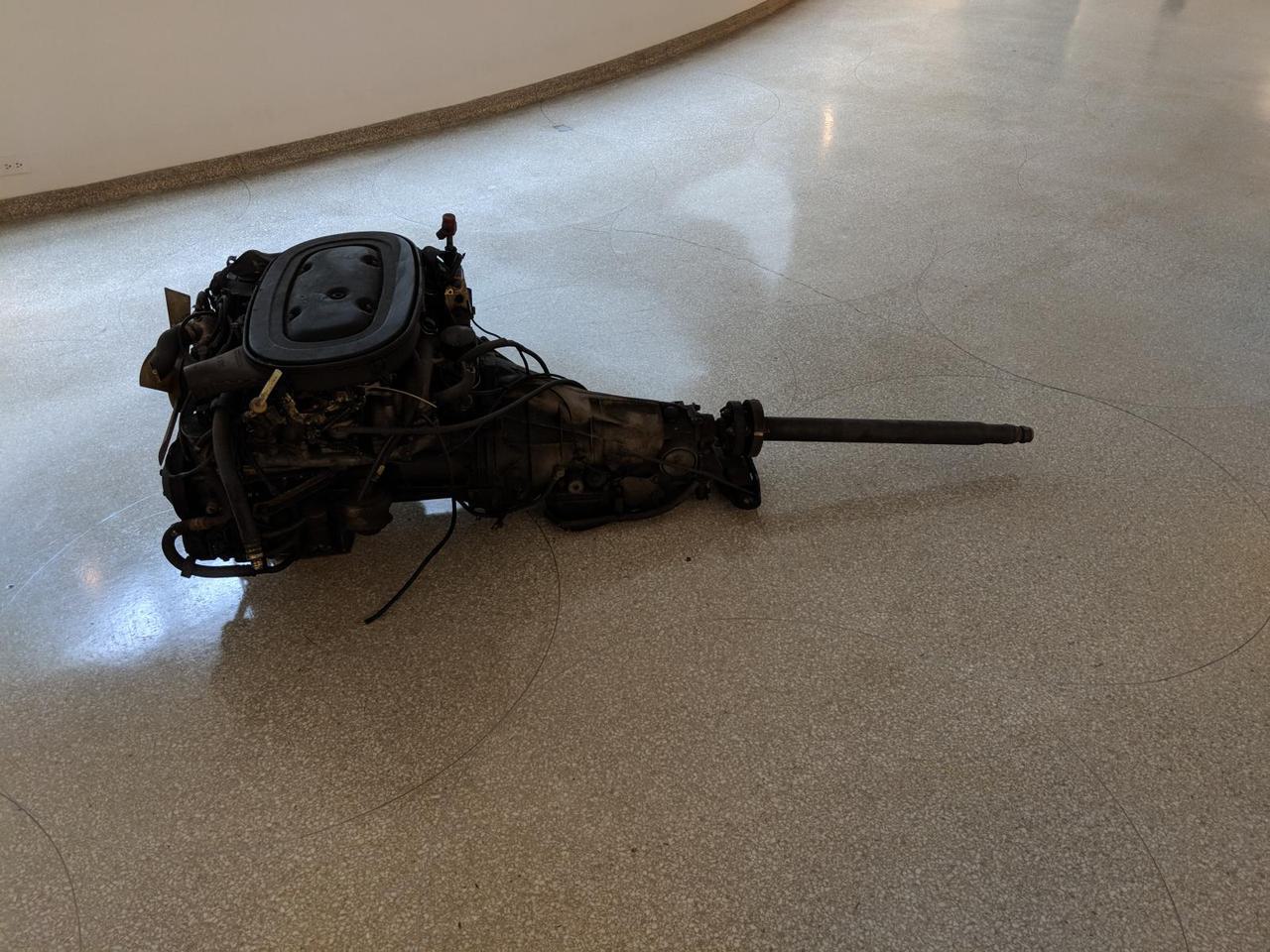 Filthy car engine that has been dumped in the middle of the museum floor.