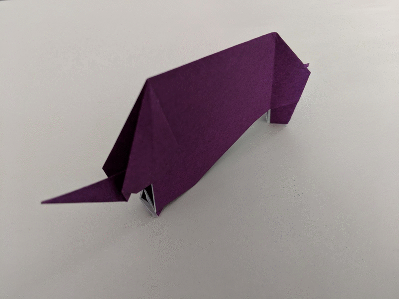 animation showing origami elephants sitting on a white piece of paper. The elephants are made with purple, orange and blue paper.