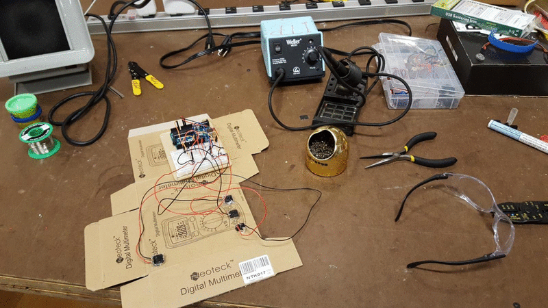 animation showing a few steps in the assembly of the device. The first two show a breadboard with lots of wires sitting on cardboard. The third shows the cardboard assembled as a normal cardboard box, containing the breadboard and wires inside.
