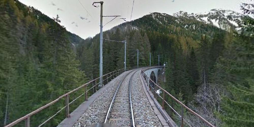 Swiss Alps with train tracks in center, veering off to the right, with trees on the sides and snow covered mountains in the background.