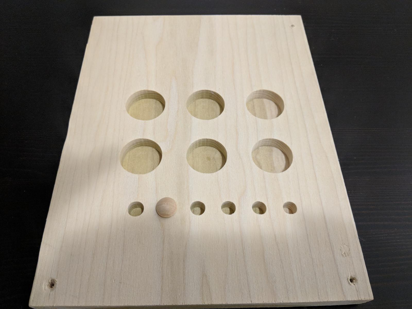 rectangle piece of wood with large and small circles cut into it.