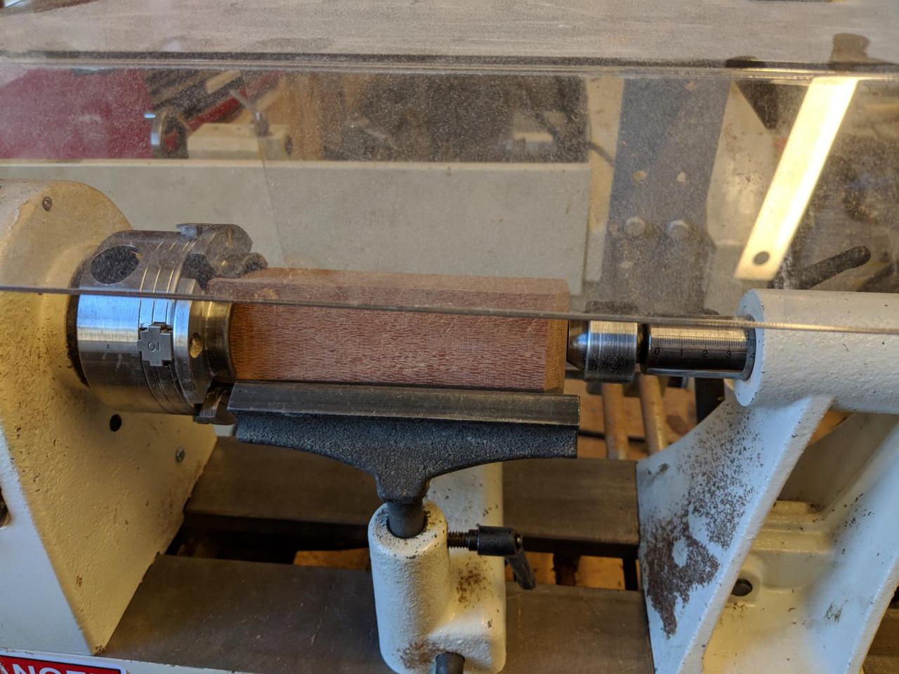wooden block mounted in wood lathe with metal edge, called a banjo, near the wooden block.