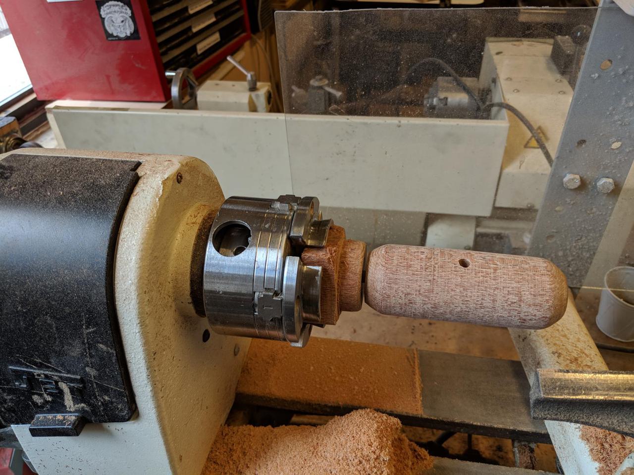 wood mounted on wood lathe with tiny piece connecting mallet head from the wood that is connected to the four-jaw chuck.