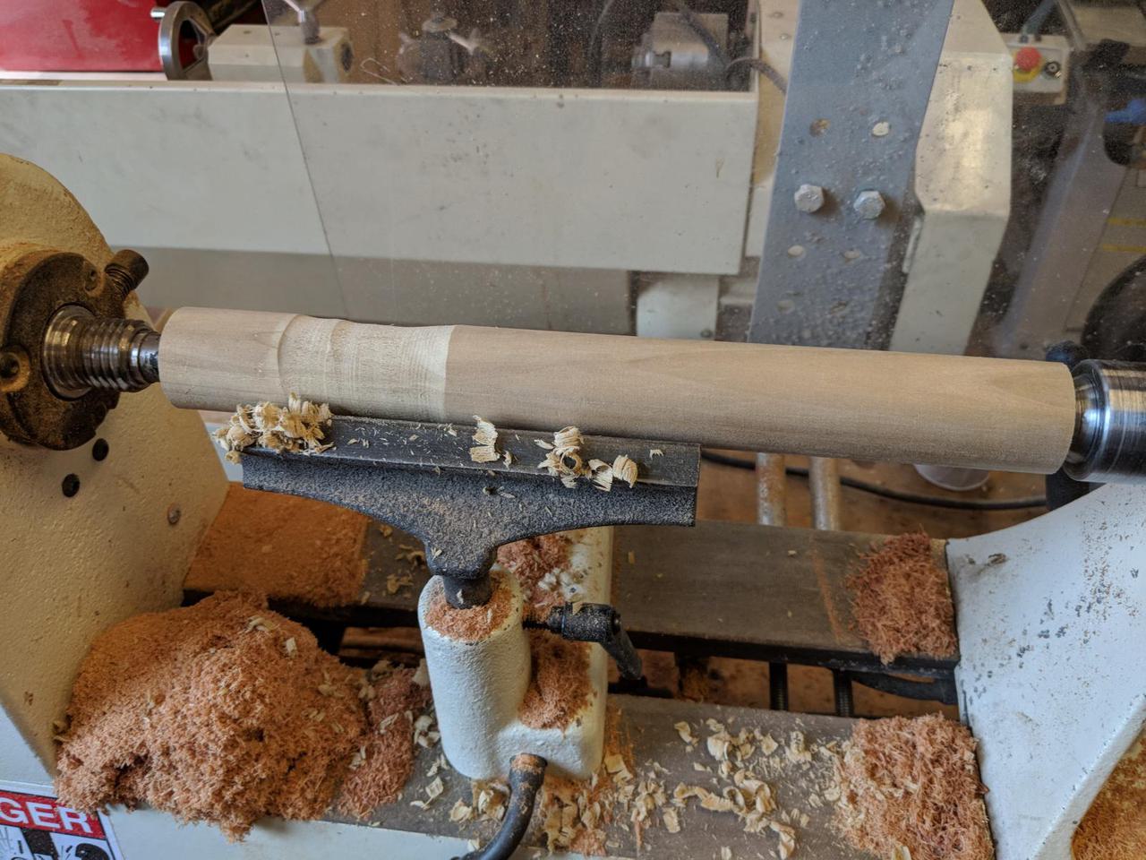 wooden cylinder in wood lathe with some wood carved out of it.