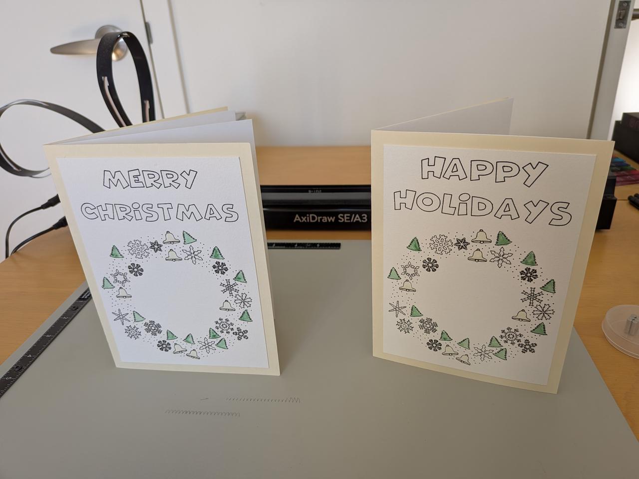 two holiday cards with a christmas wreath on each and the words "happy holidays" or "merry christmas" across the top