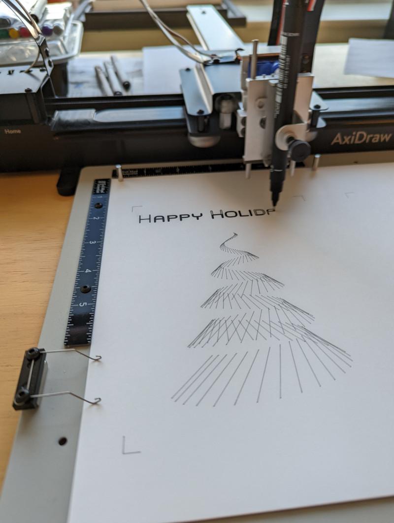 axidraw pen plotter drawing a wire frame christmas tree and the words "happy holidays" across the top