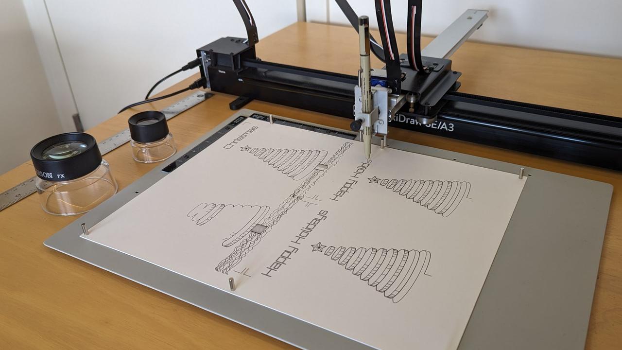 axidraw pen plotter drawing four christmas tree cards and with the words "happy holidays" or "merry christmas" across the top of each