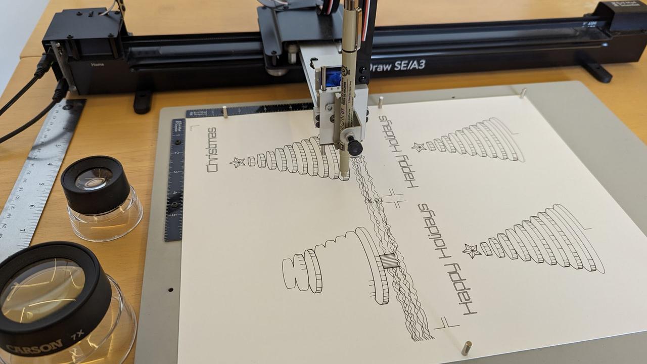 axidraw pen plotter drawing four christmas tree cards and with the words "happy holidays" or "merry christmas" across the top of each